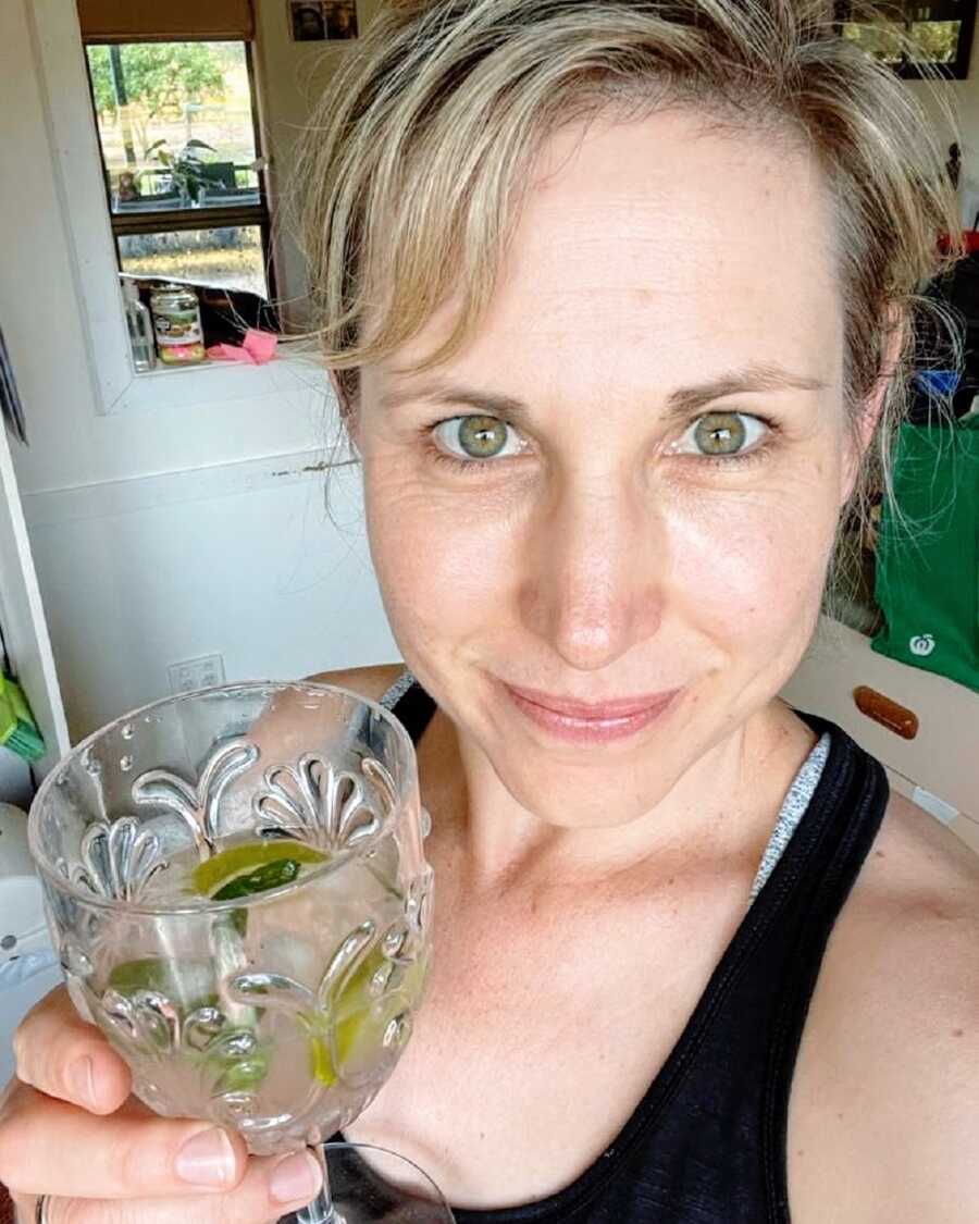 A mom holding a glass of alcohol wearing a black tank top