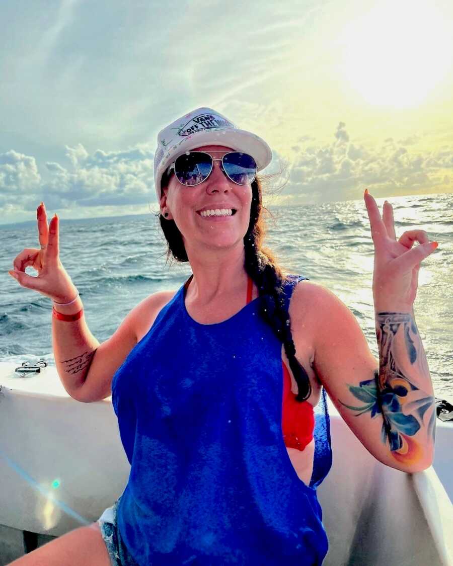sober woman smiles wide on a boat throwing up peace signs