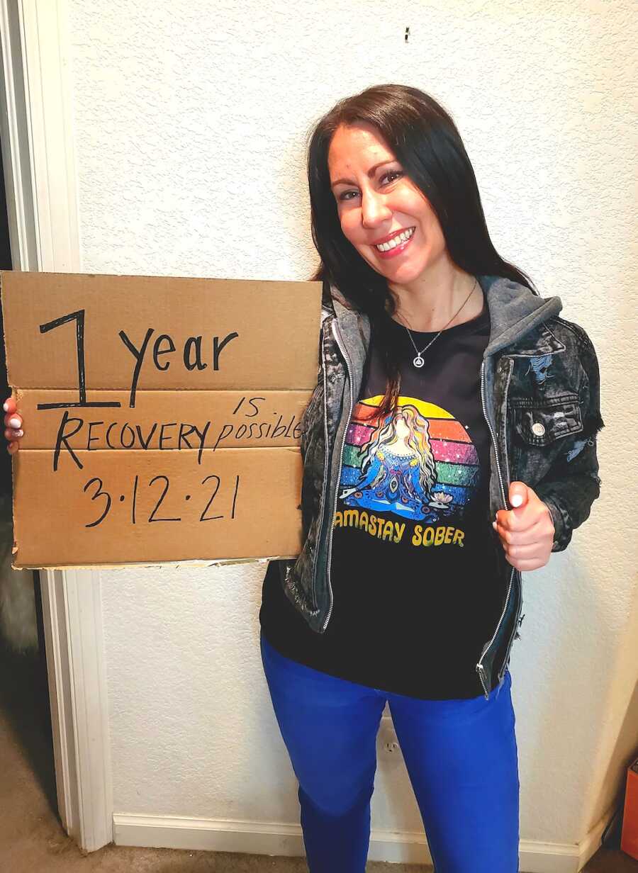 woman holds up sign saying she has been sober for one year