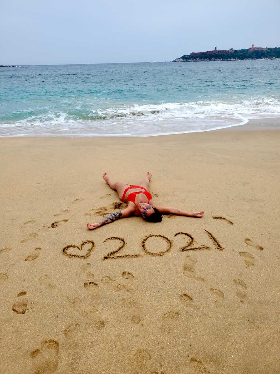 sober woman lays in the sand with 2021 written above her