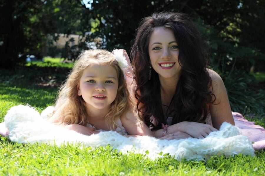 mother lays on grass with a blanket next to her daughter