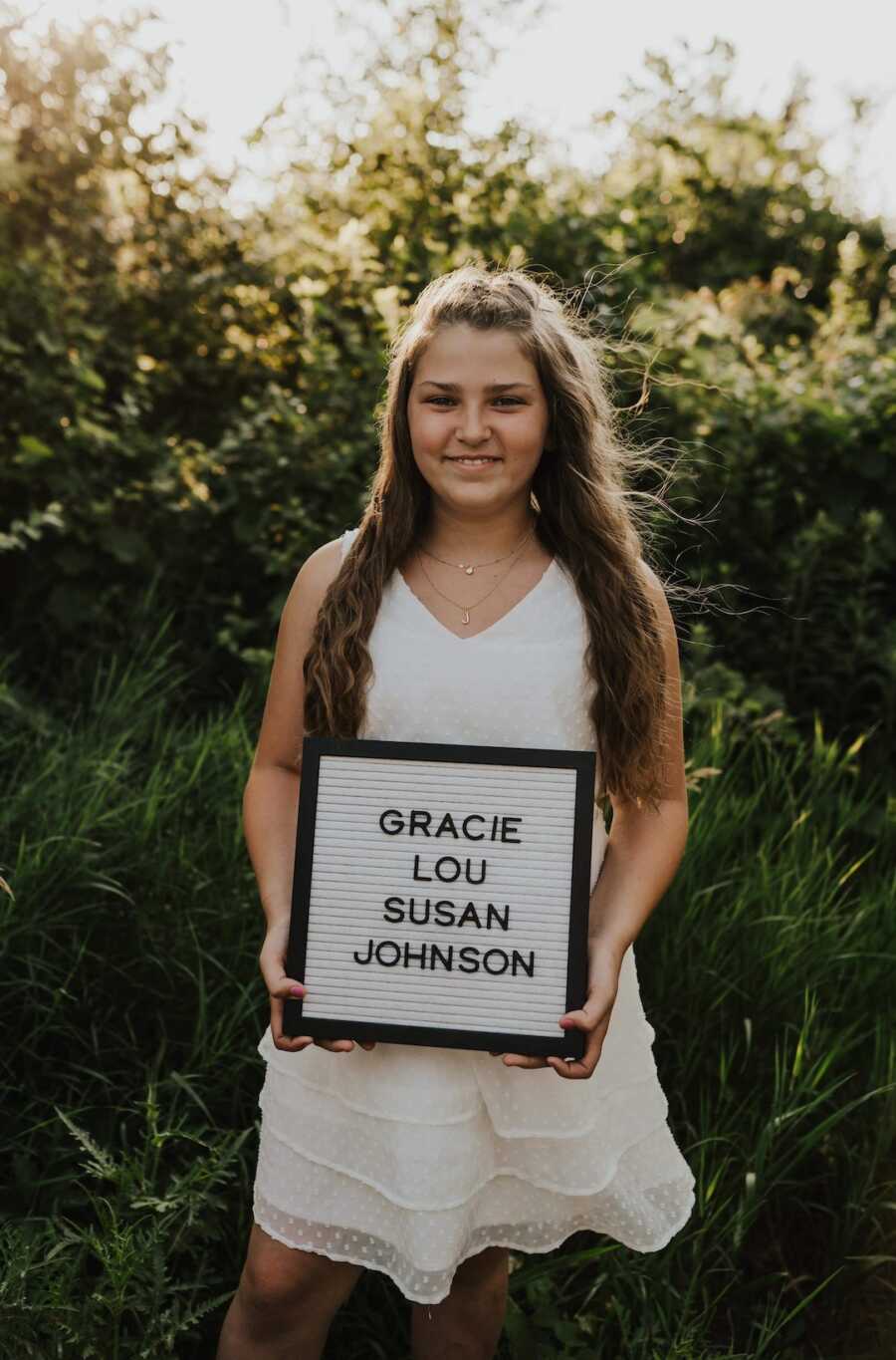 Adopted daughter stands holding a letter sign