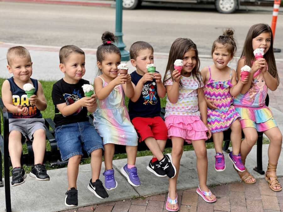 7 children, 5 being quintuplets, sit on bench eating ice cream cones