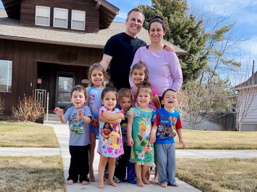 family of mom, dad, two older children and quintuplets stand together outside of their home