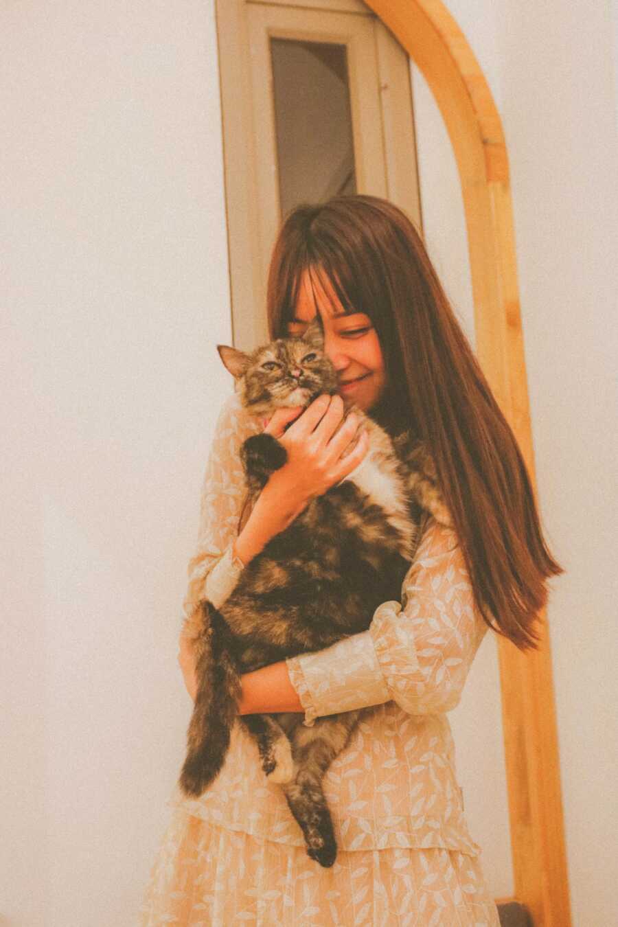 woman holds her cat close to her, putting her face on their head