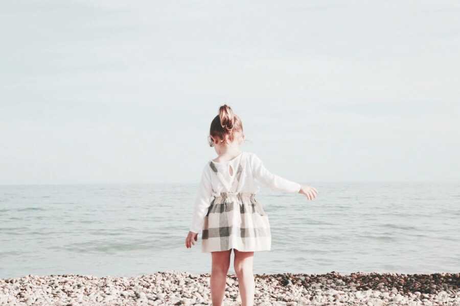 young girl faces the ocean while walking on rocks