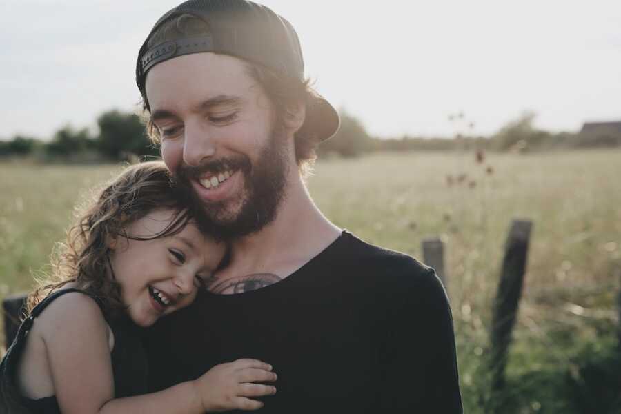 father holds his daughter on his chest, both smiling