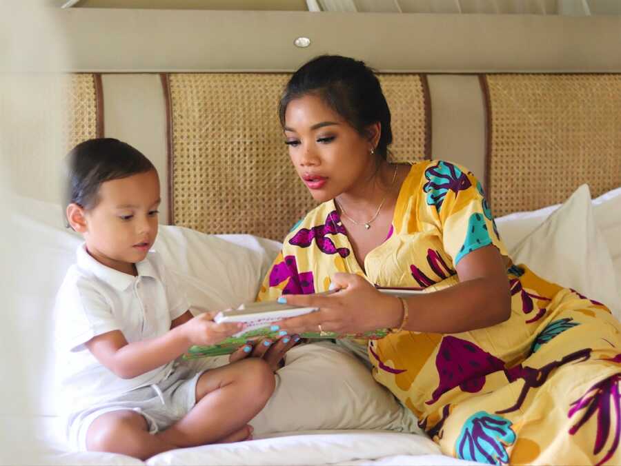 mom sits in bed with her son teaching him how to read