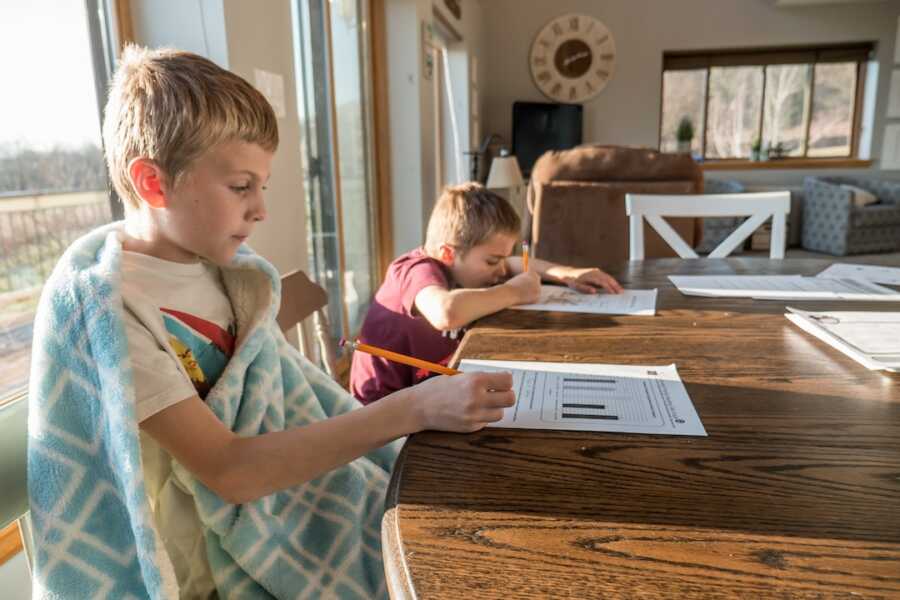 two boys sit at the kitchen table doing school