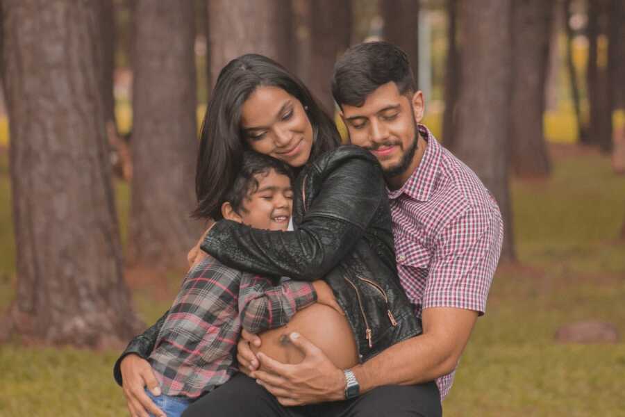 husband wraps his arms around his pregnant wife and son