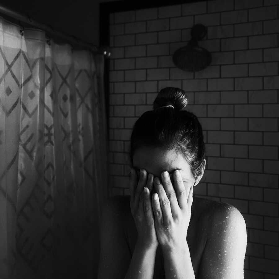 woman stands in the shower with running water and her hands over her face