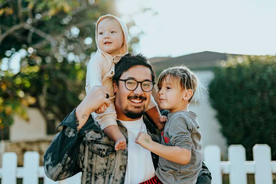 father holds one child in his arms and the other on his shoulders