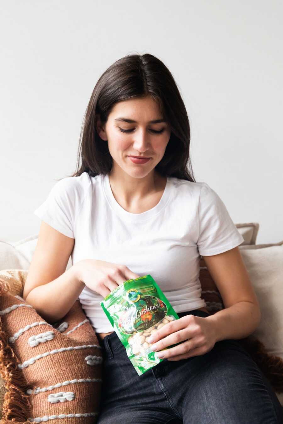 woman sits on the couch eating a snack