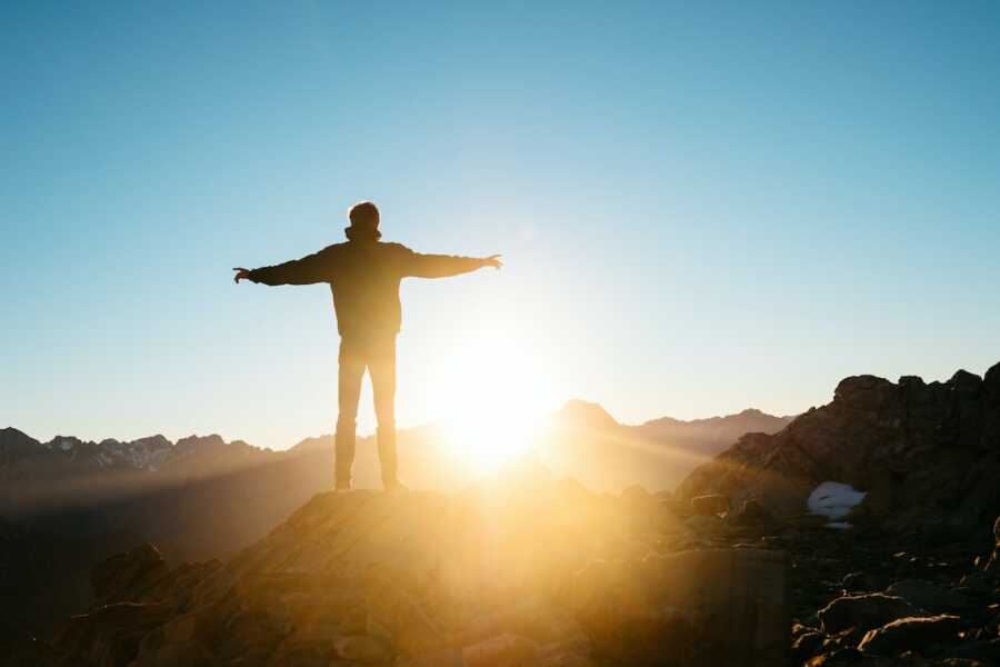 man stands with his hands outstretched facing the horizon