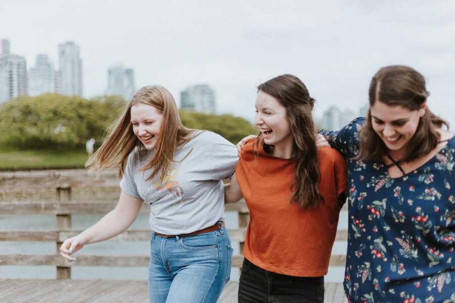 three friends hold onto one another while walking, laughing