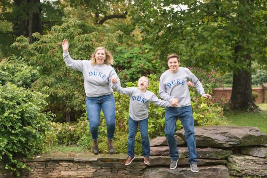 adoptive parents and their son jump off wall together, wearing matching shirts