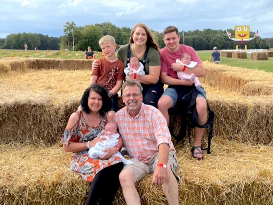 parents sit with their adopted son, biological triplets, and parents on hay bales