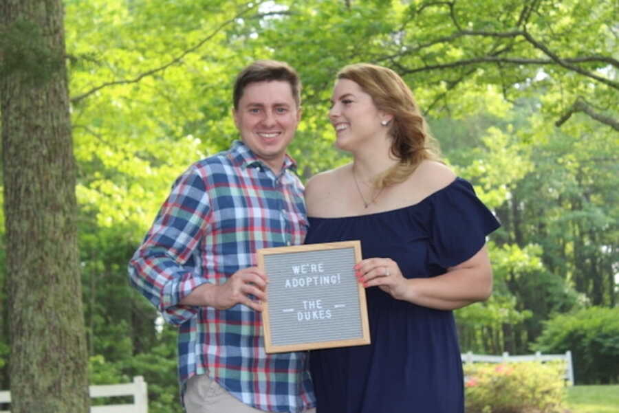 couple holds sign together announcing that they are adopting to grow their family