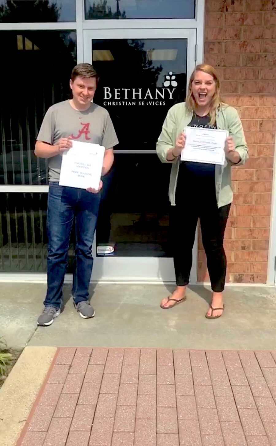 couple stands in front of agency after completing foster care adoption training