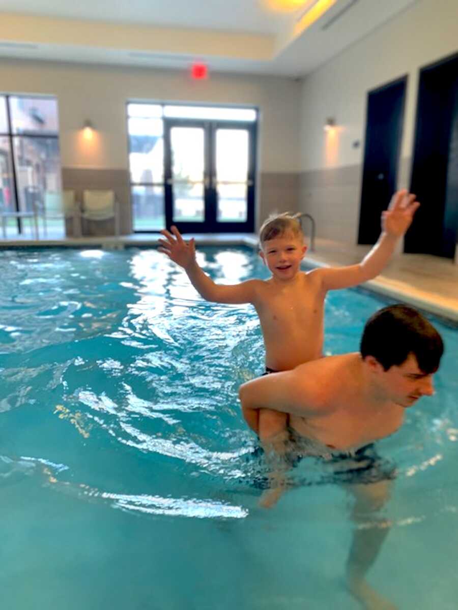 adoptive father holds his son on his back while in the pool