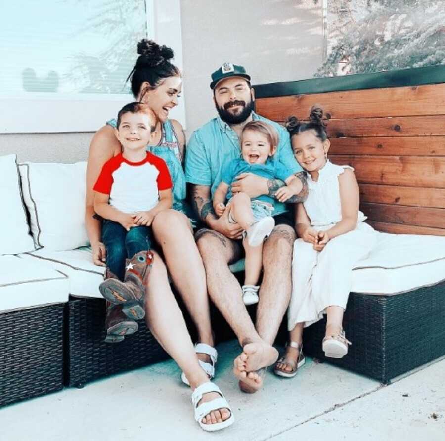 Blended family takes picture together on porch bench.