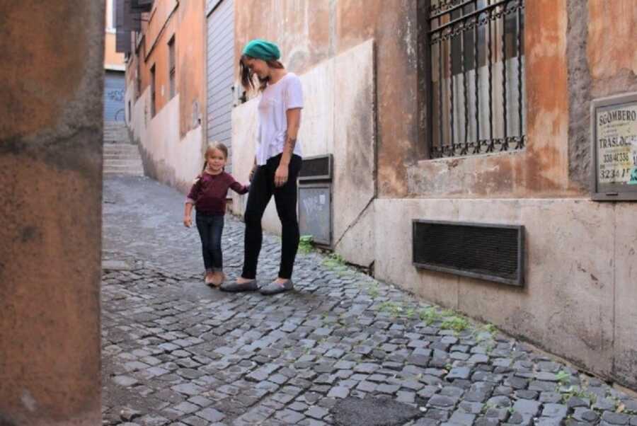 Single mom and young daughter take picture in alley.