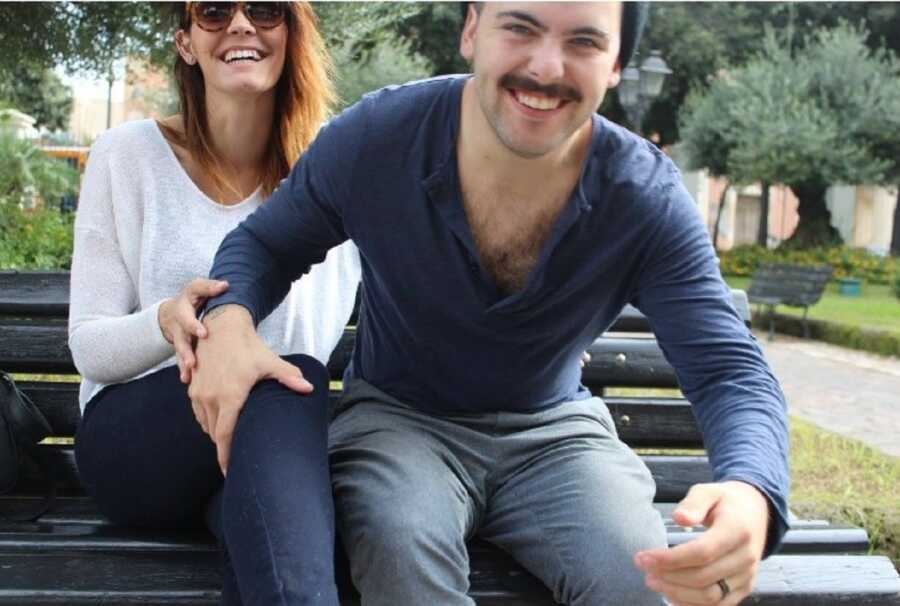 Man leans forward laughing with hand on woman's knee.