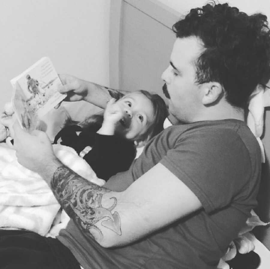 Boyfriend holds baby girl and reads her a story.