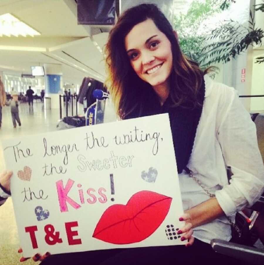 Woman holds sign waiting for military husband's return.