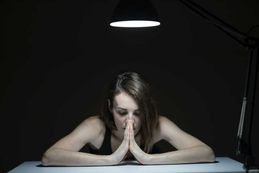 woman sits at table hands to her mouth looking down