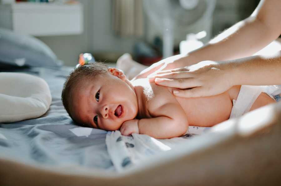 baby lays on it's stomach while mother puts lotion on them