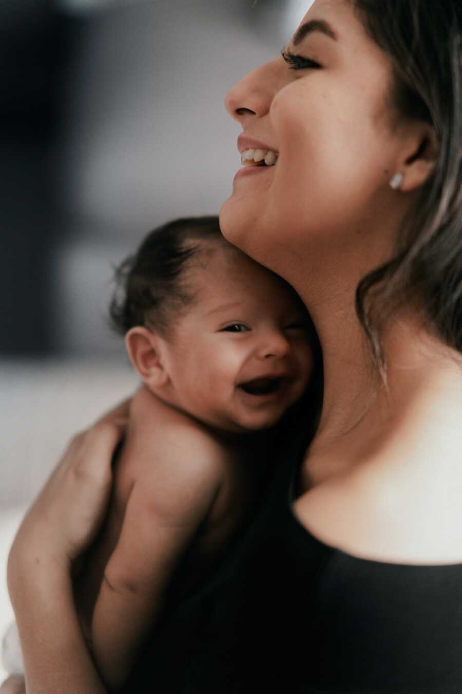 mother smiles wide while holding her baby on her chest