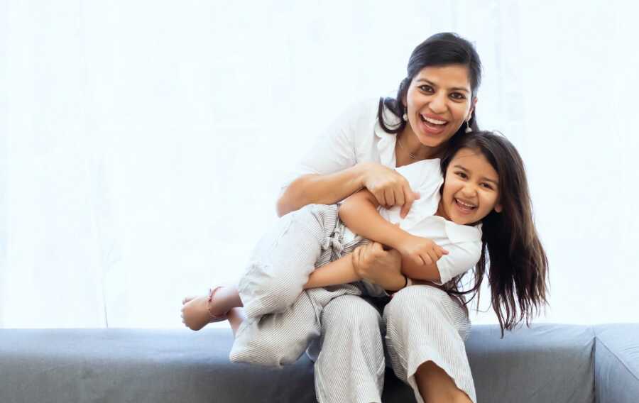 mother holds her daughter on her lap tightly, both smile wide