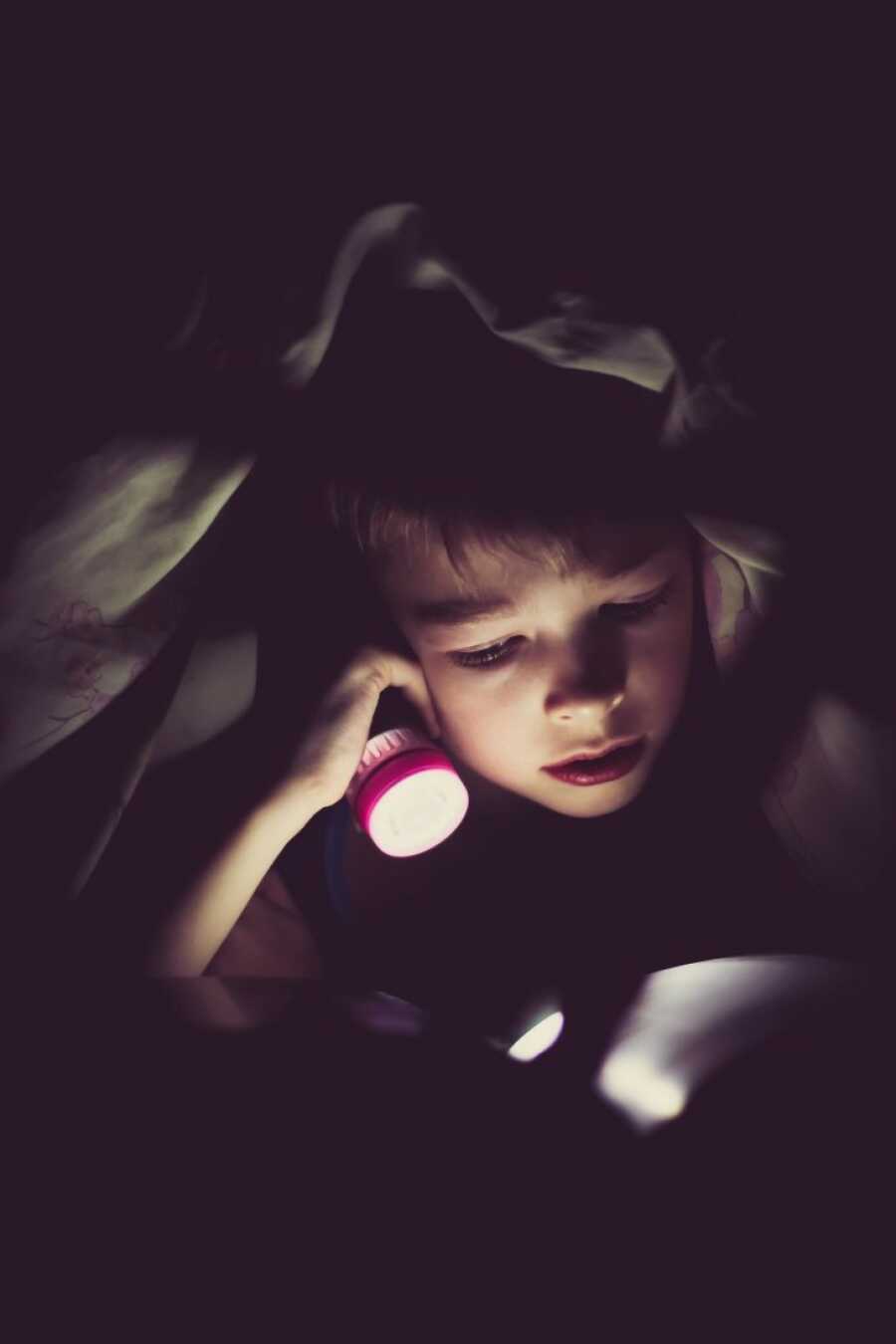 kid using a flash light to read stories