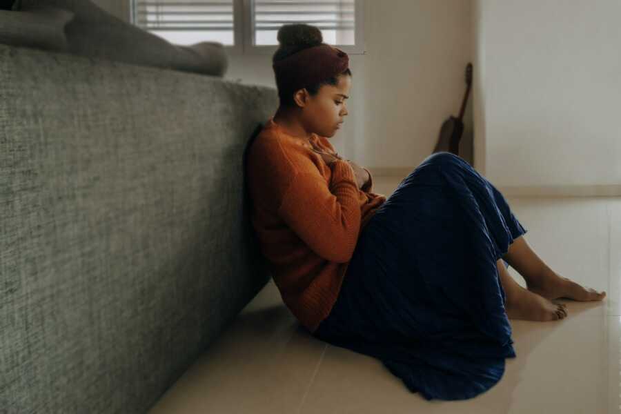 woman sits alone at the foot of her bed