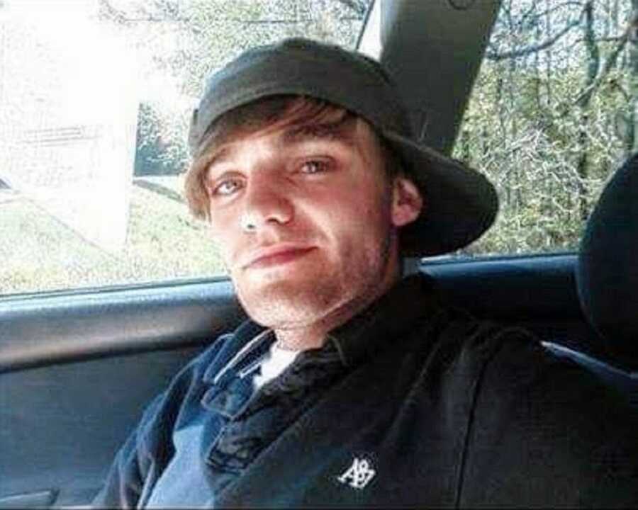 A young man wearing a baseball hat backwards sits in a car