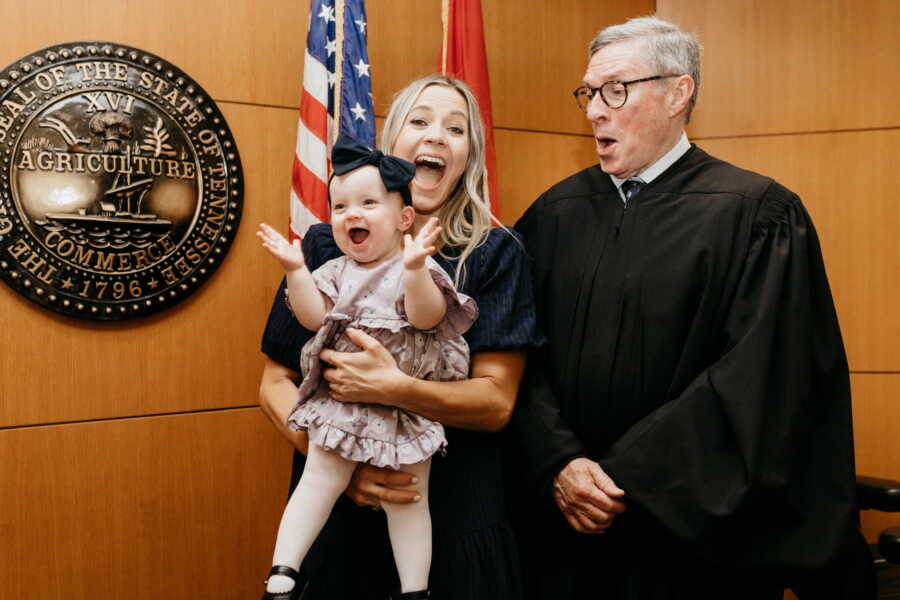 Single mom and baby girl take happy picture with judge upon finalizing adoption.