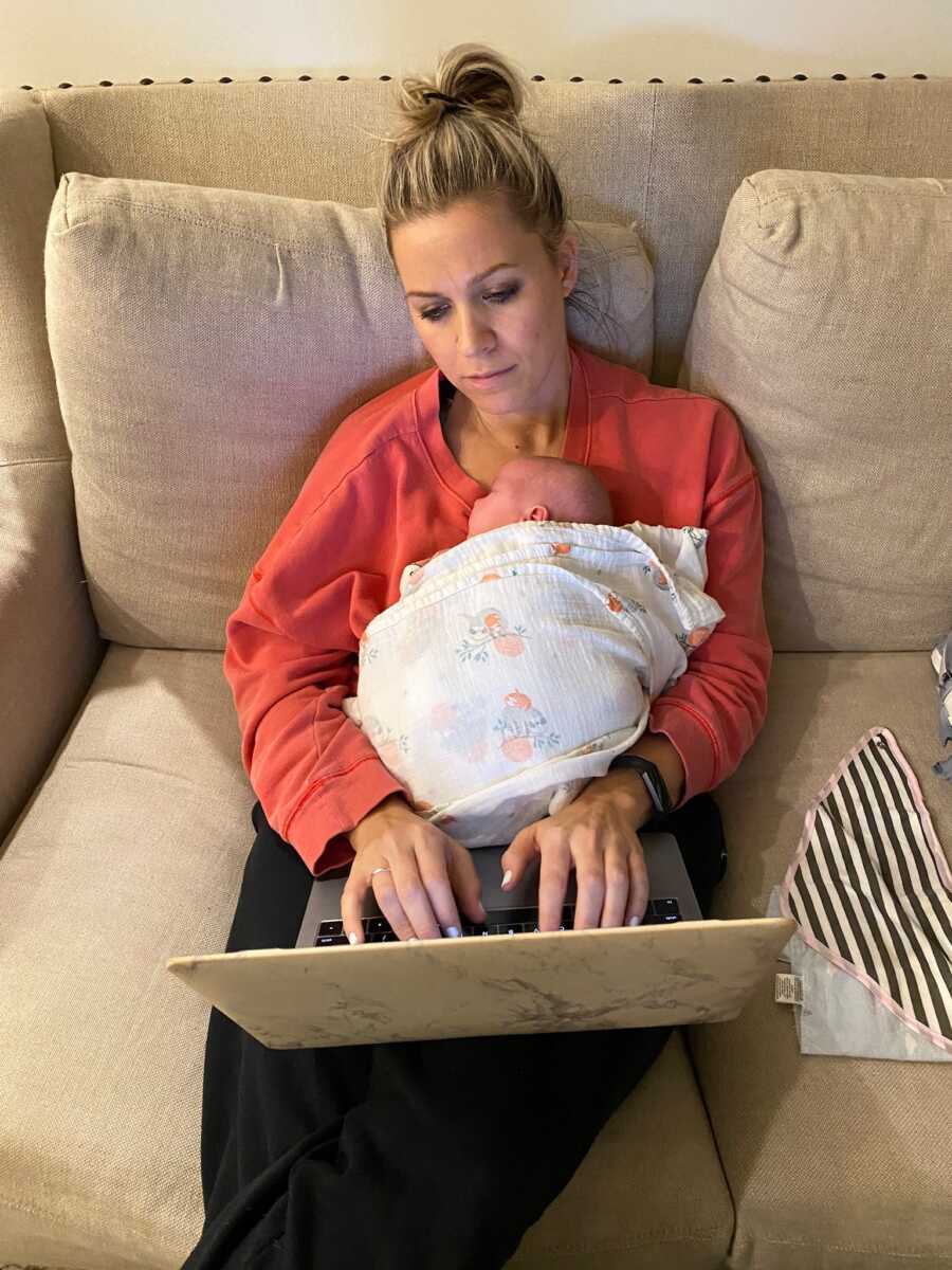 Single foster mom types on her laptop while sleeping baby girl lays on her chest.