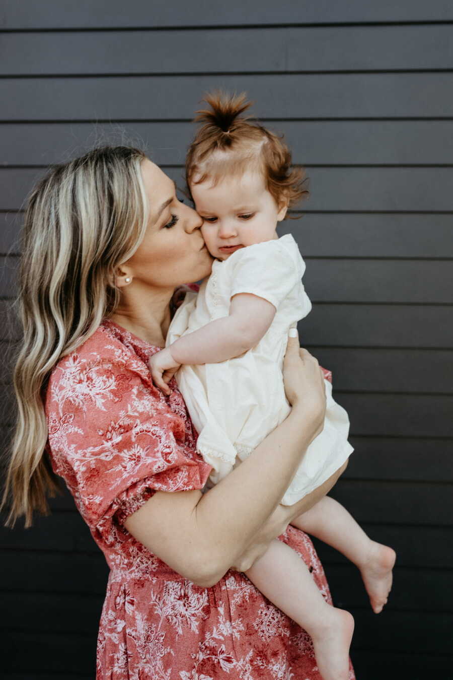 Single adoptive mom kisses baby girl's cheek as she holds her close against her chest.