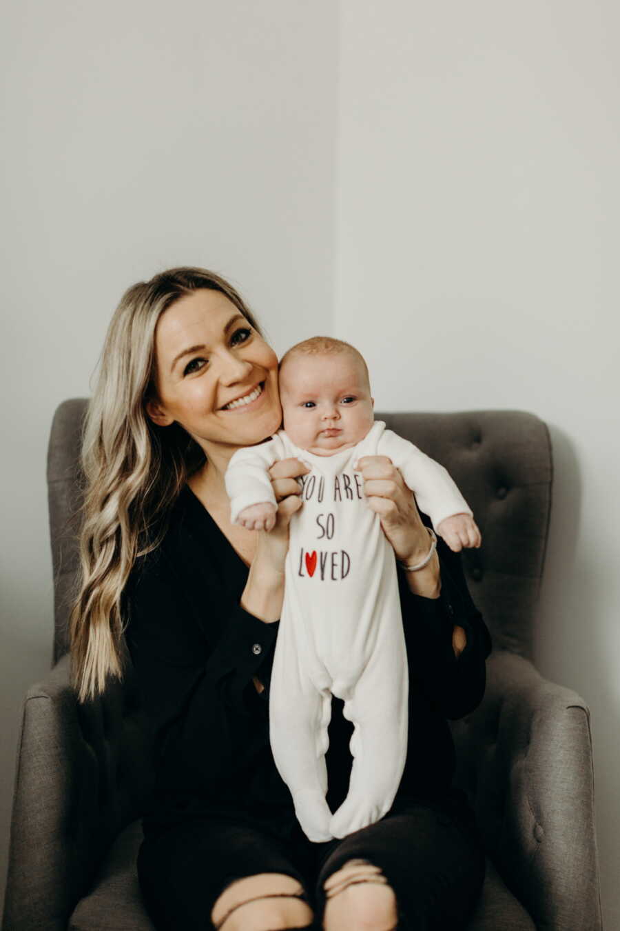 Foster mom holds up baby girl and smiles with faced pressed against her cheek.