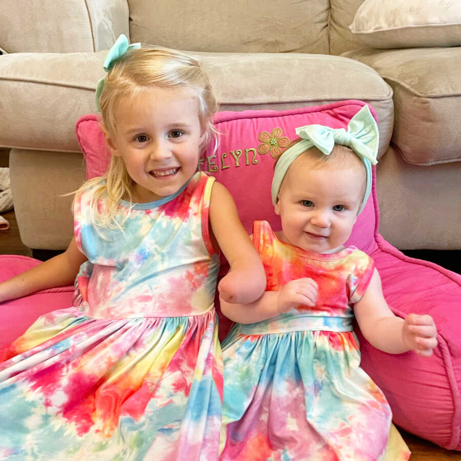 Young girl with limb difference sits with her baby sister.