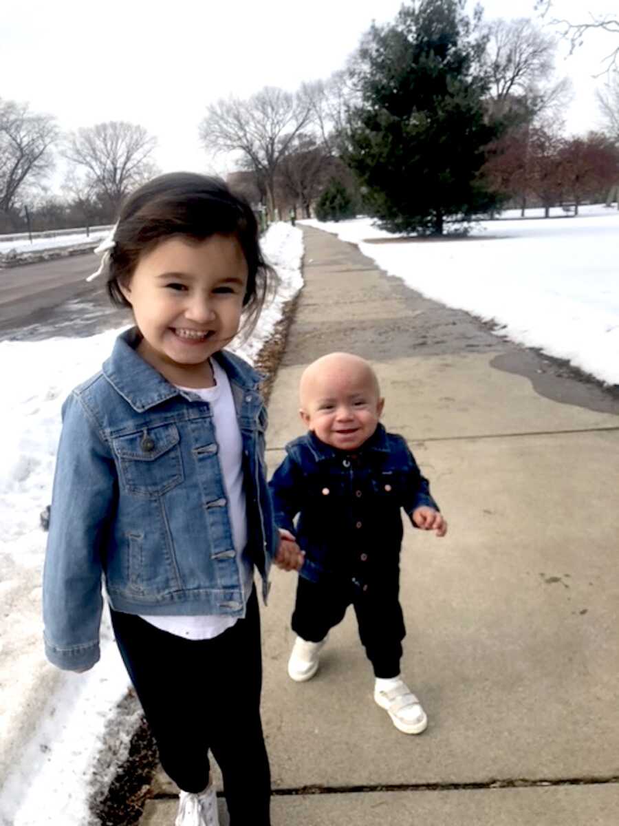 big sister holds her brothers hand while they walk