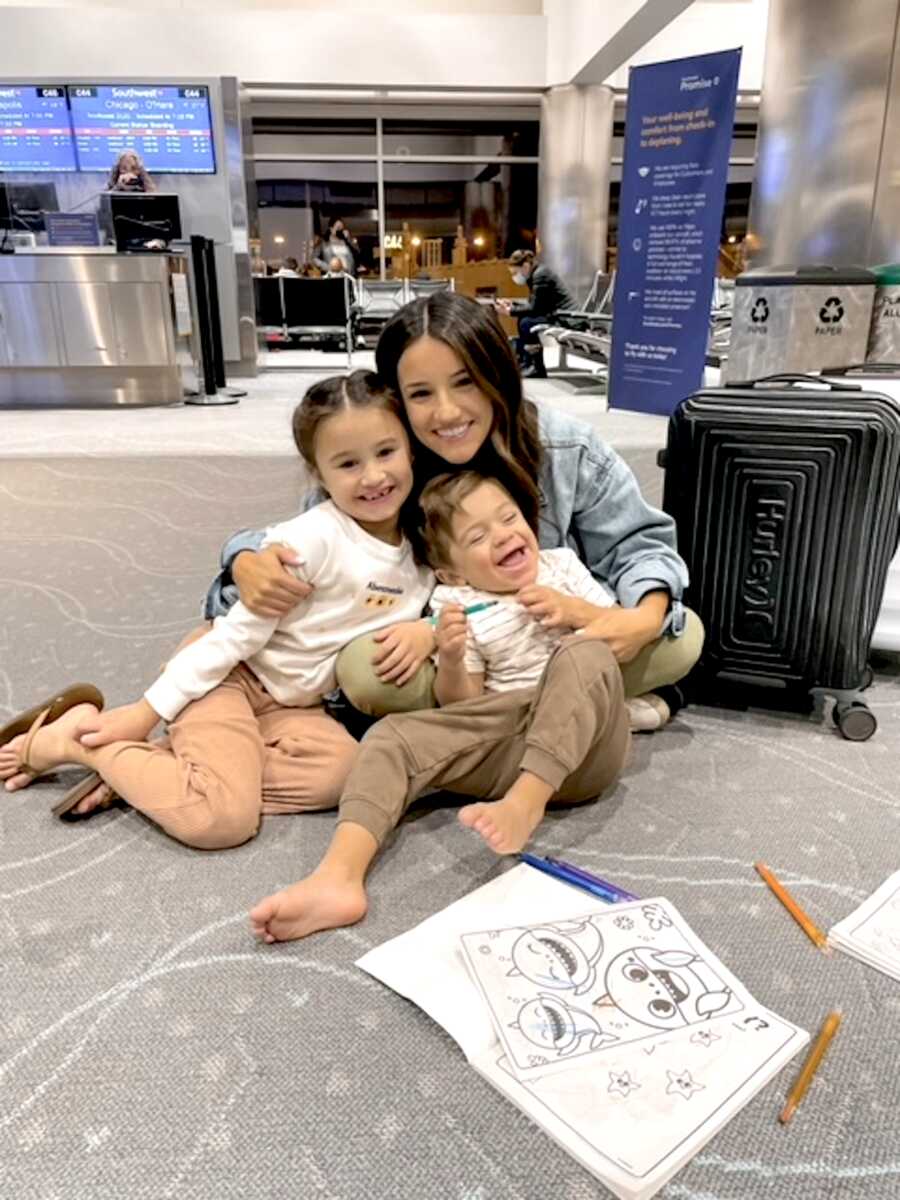 mom sits on floor of airport with her two children