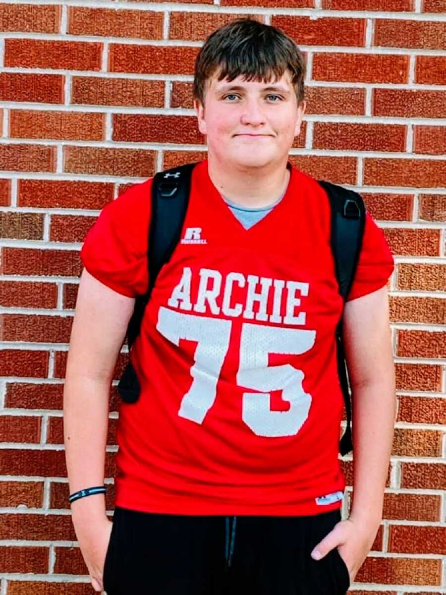 A boy wearing a red jersey number 75 leaning against a brick wall