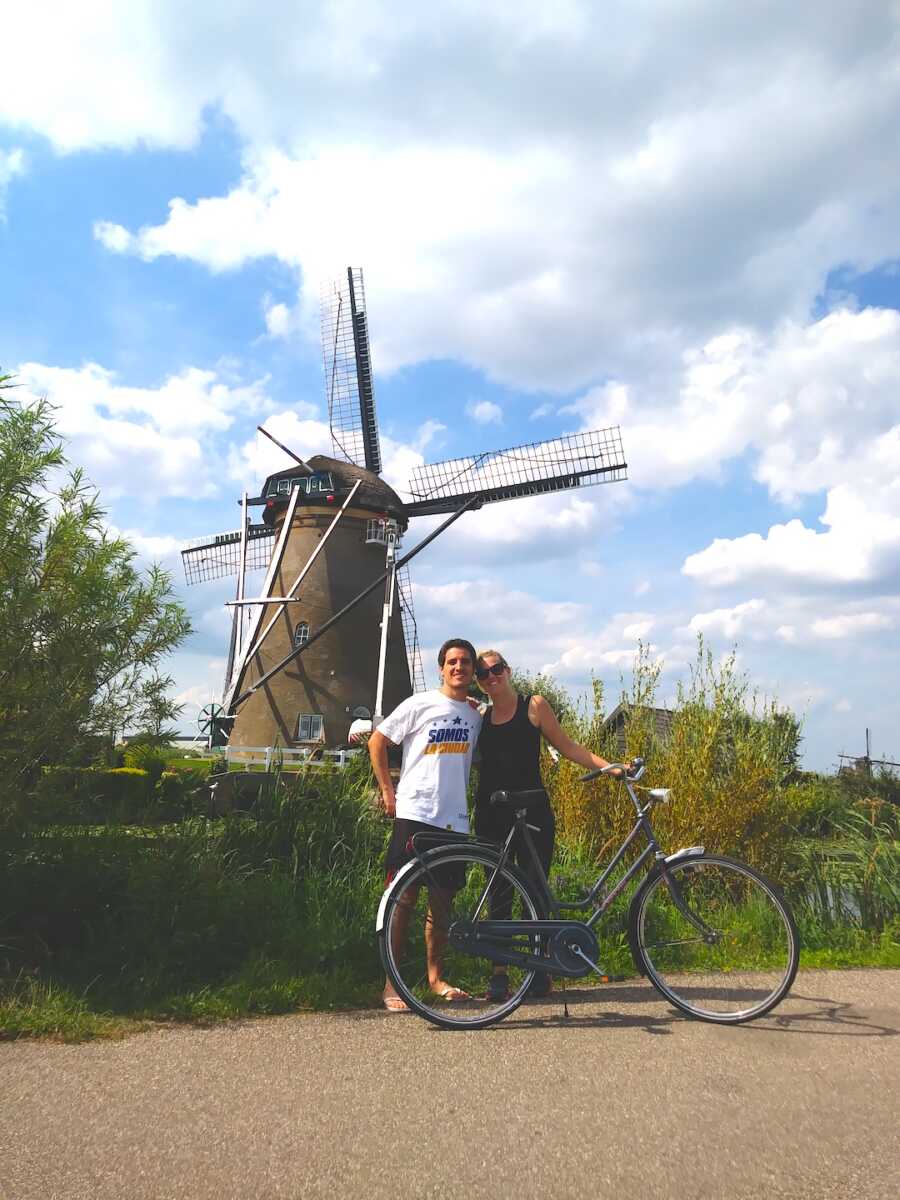 husband and wife stand with a bike in front of a windmill