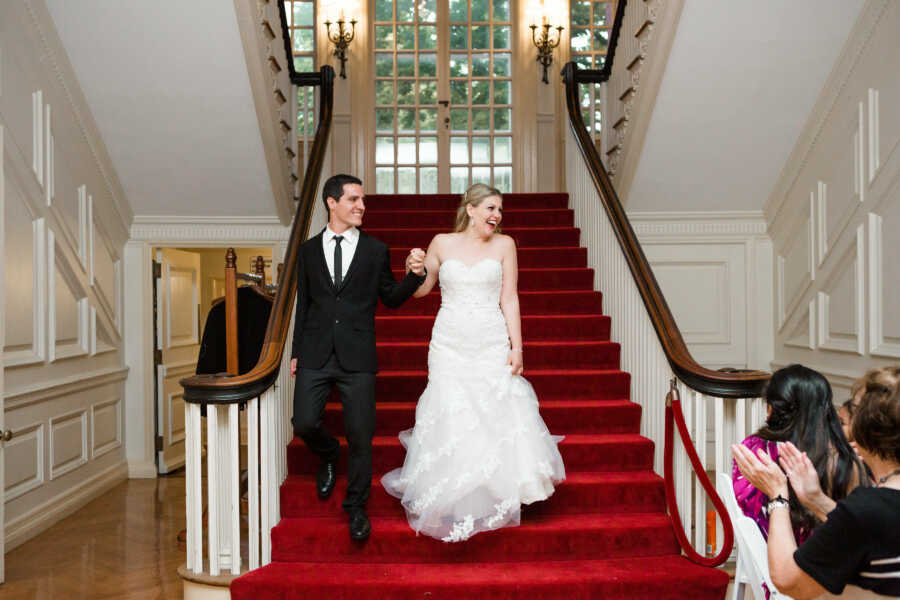 husband and wife walk down stairs holding hands on their wedding day