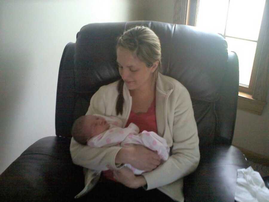 New mom holds baby girl while sitting in black leather recliner.