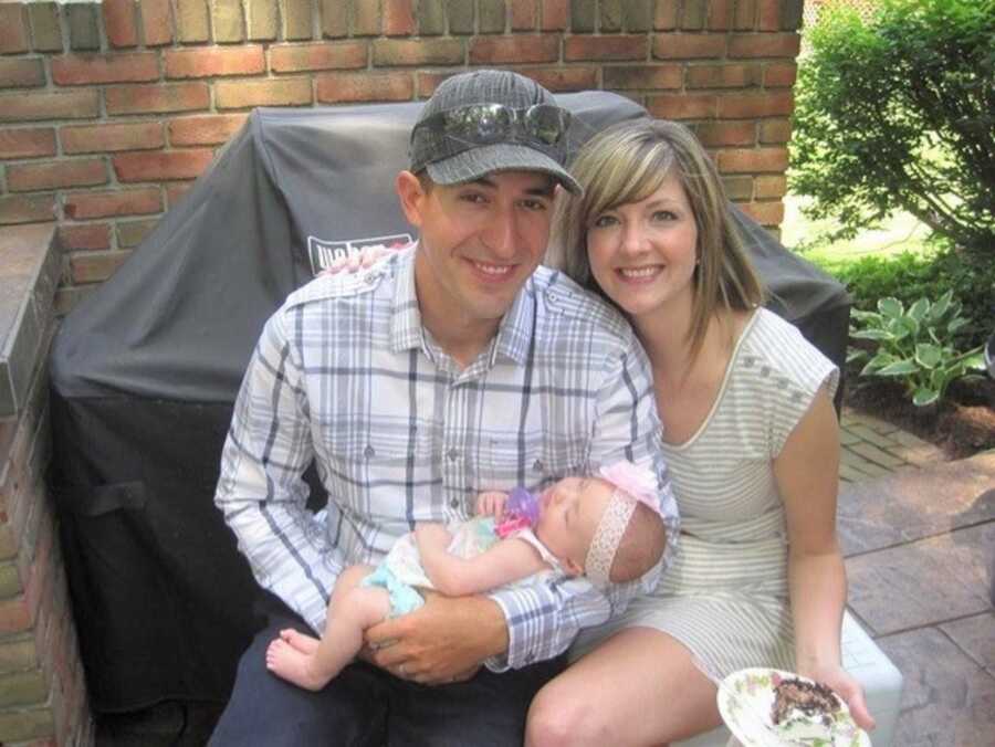 Young couple hold new baby girl, sitting outside together.