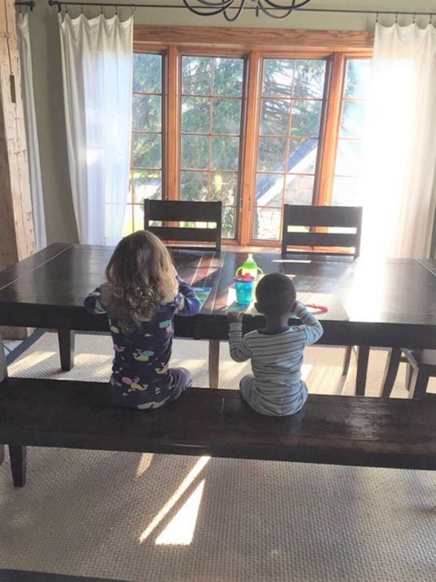Couple's daughter and first foster placement sit side by side at kitchen table.