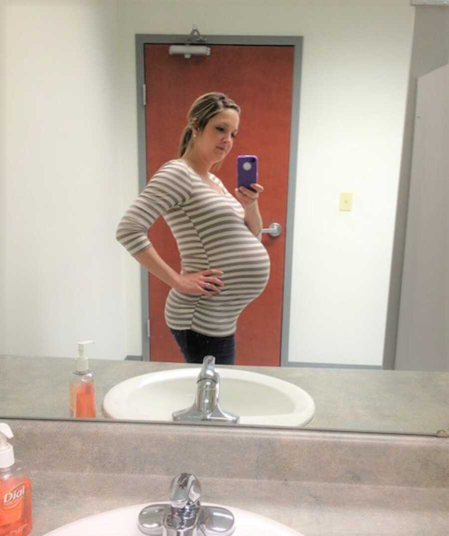 Young woman takes bathroom selfie of pregnant belly.